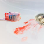 Closeup of a toothbrush with blood on it and in the sink from gum disease