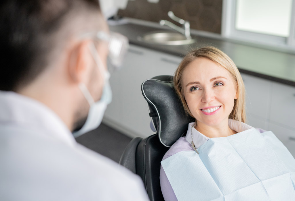 Blonde woman smiles while sitting in the dental chair before root canal therapy to save your infected tooth