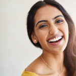 Brunette woman in a yellow shirt smiles after receiving professional teeth whitening in San Antonio, TX