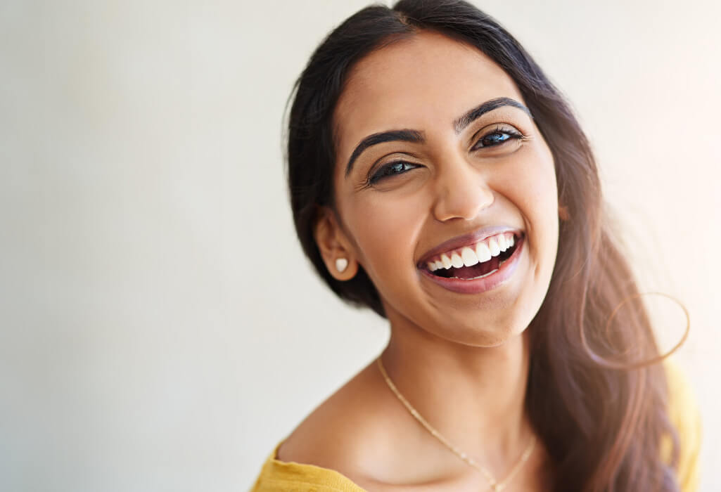 Brunette woman in a yellow shirt smiles after receiving professional teeth whitening in San Antonio, TX