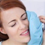 woman holds an ice pack to her cheek after oral surgery