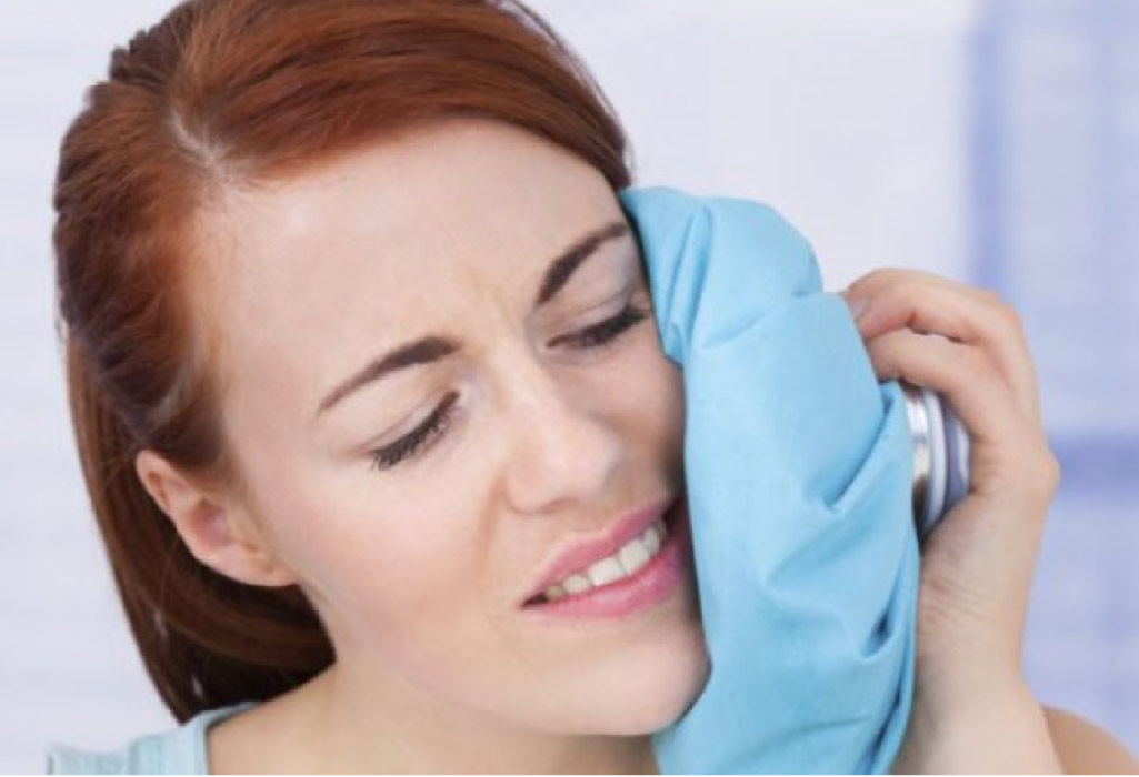 woman holds an ice pack to her cheek after oral surgery