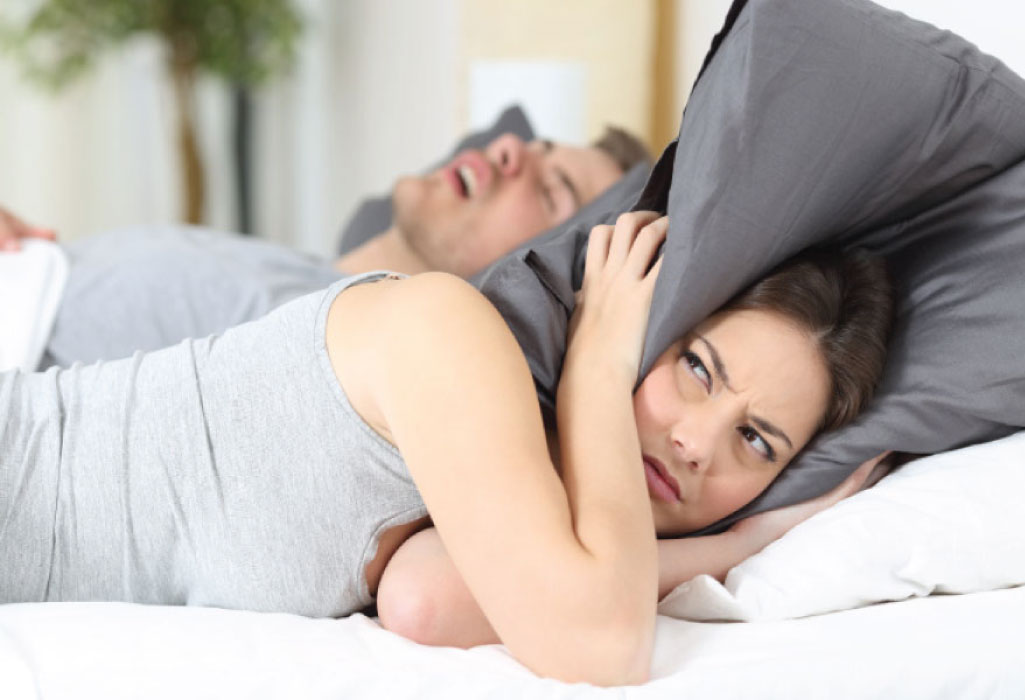 woman covers her head with a pillow to block out her partners sleep apnea snoring