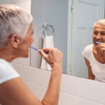 woman looks in the mirror to brush her teeth to maintain good gum health