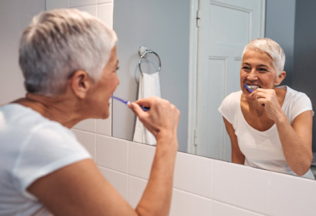 woman looks in the mirror to brush her teeth to maintain good gum health