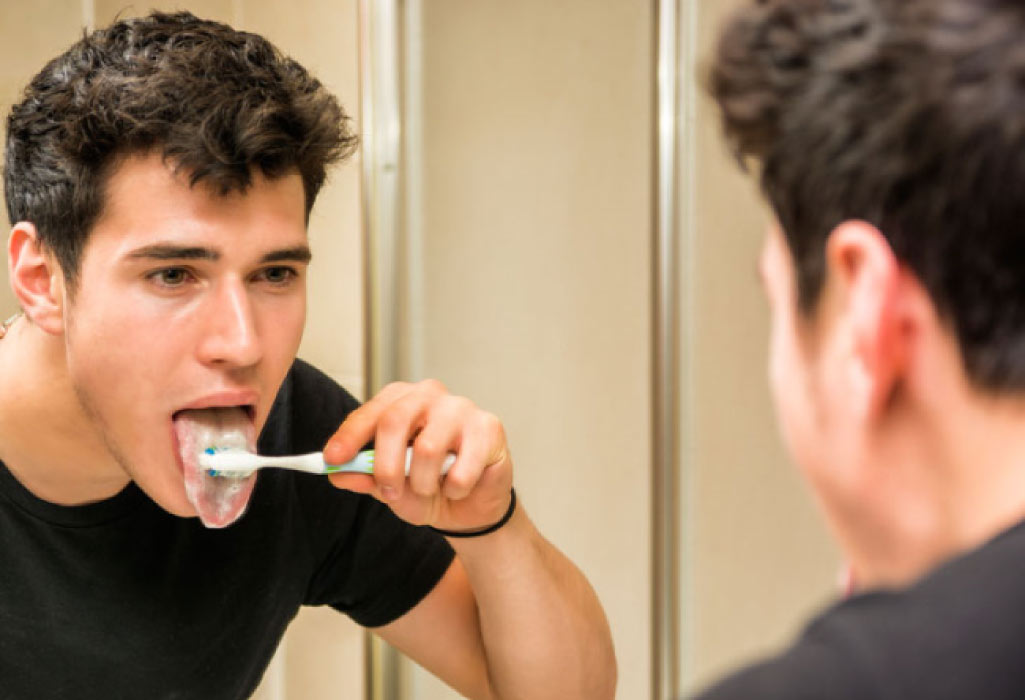 young man brushes his tongue to prevent bad breath