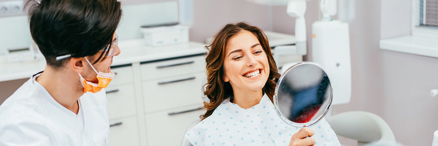 woman examining her bright, white smile in a mirror at the dentist's office