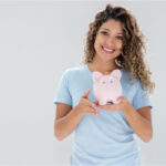young woman holds a piggybank and smiles after learning about affordable dental plans