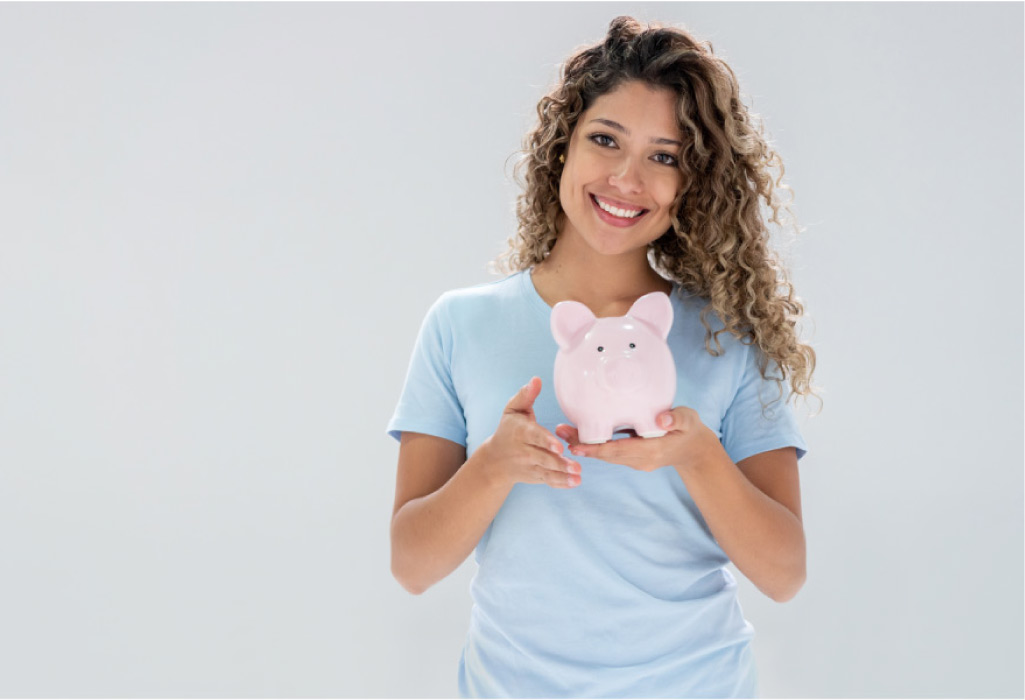 young woman holds a piggybank and smiles after learning about affordable dental plans