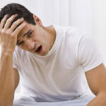 man sitting on the side of a bed holding his head after a night suffering from sleep apnea