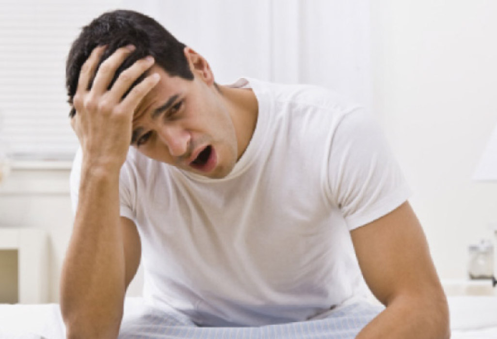 man sitting on the side of a bed holding his head after a night suffering from sleep apnea