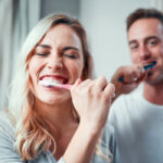 young couple brushing their teeth together with fluoride toothpaste