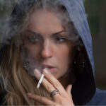 woman wearing a hoodie smokes a cigarette