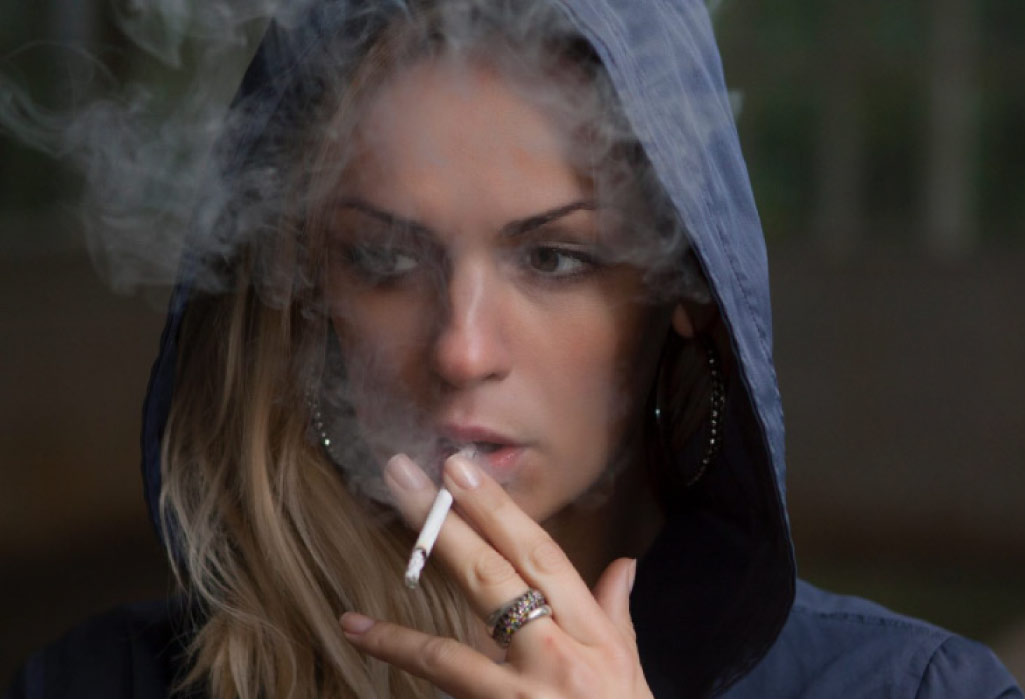 woman wearing a hoodie smokes a cigarette