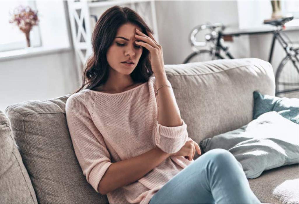 young woman sitting on the couch holding her head in pain from a migraine headache