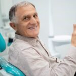 senior man sitting in the dentist chair gives a thumbs up after learning about the connection between diabetes and oral health