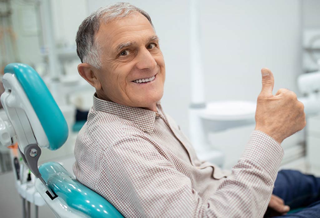 senior man sitting in the dentist chair gives a thumbs up after learning about the connection between diabetes and oral health