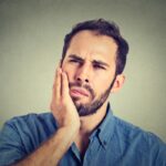 bearded man holds his jaw with gum pain