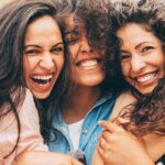 three young women hug and smile showing off their white teeth