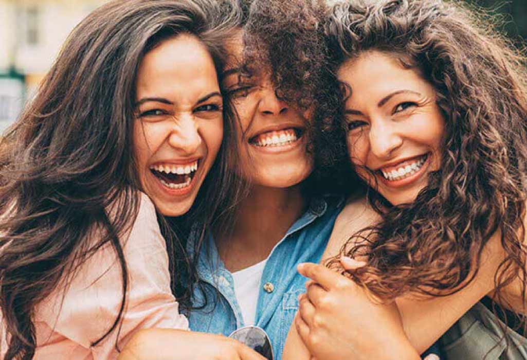 three young women hug and smile showing off their white teeth