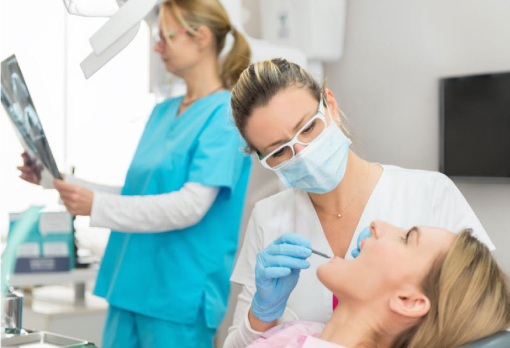 woman getting a dental checkup while a technician checks the x-rays