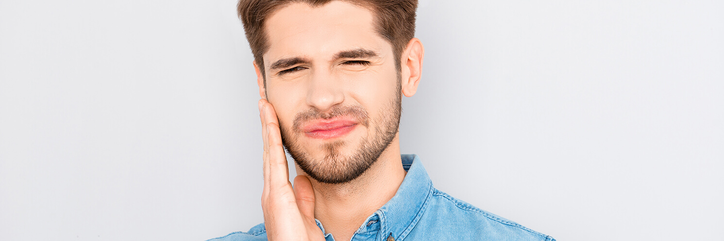 White man touching his cheek due to dental pain.