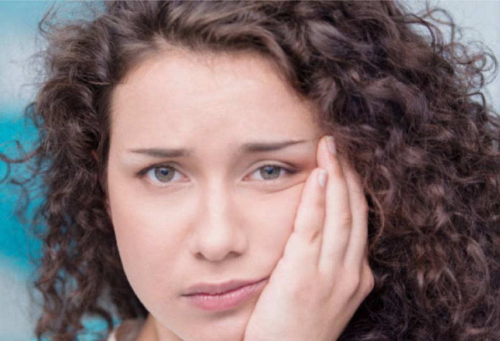 young woman holds her cheek in pain from emerging wisdom teeth