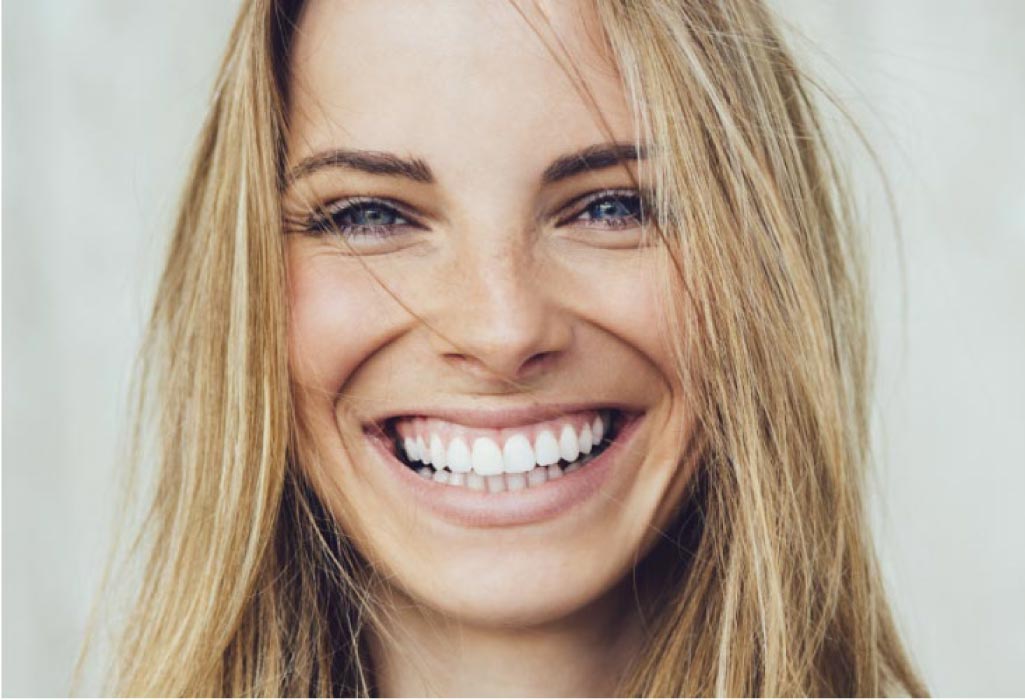 young woman smiles showing off her porcelain veneers