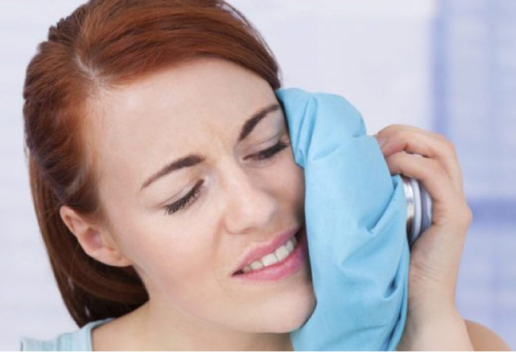 woman holds an icepack to her jaw after wisdom teeth removal