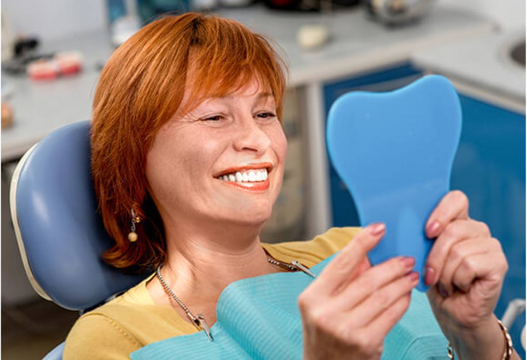 female dental patient looks in a mirror at her new snap on smile.