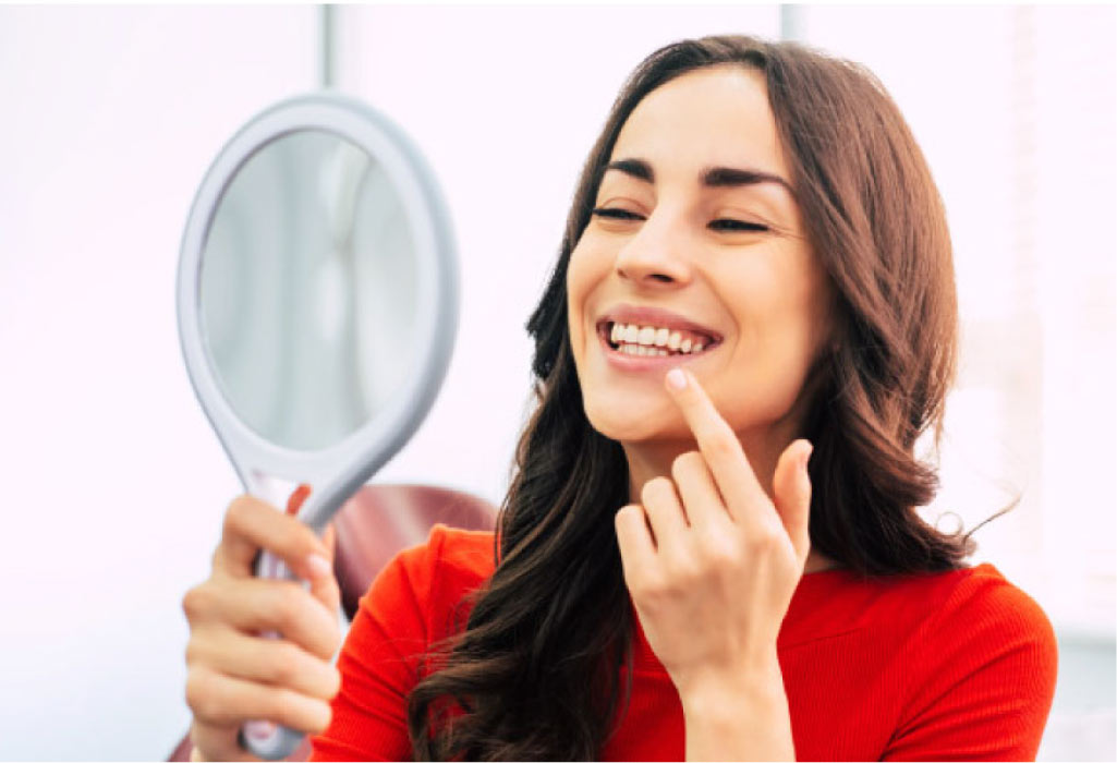 young woman inspects her gums in a handheld mirror