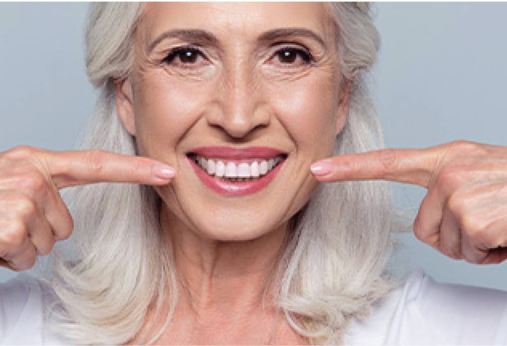 woman points with both index fingers to her dental veneer smile