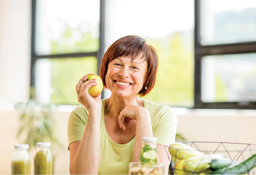 woman surrounded by healthy foods holds and apple and smiles