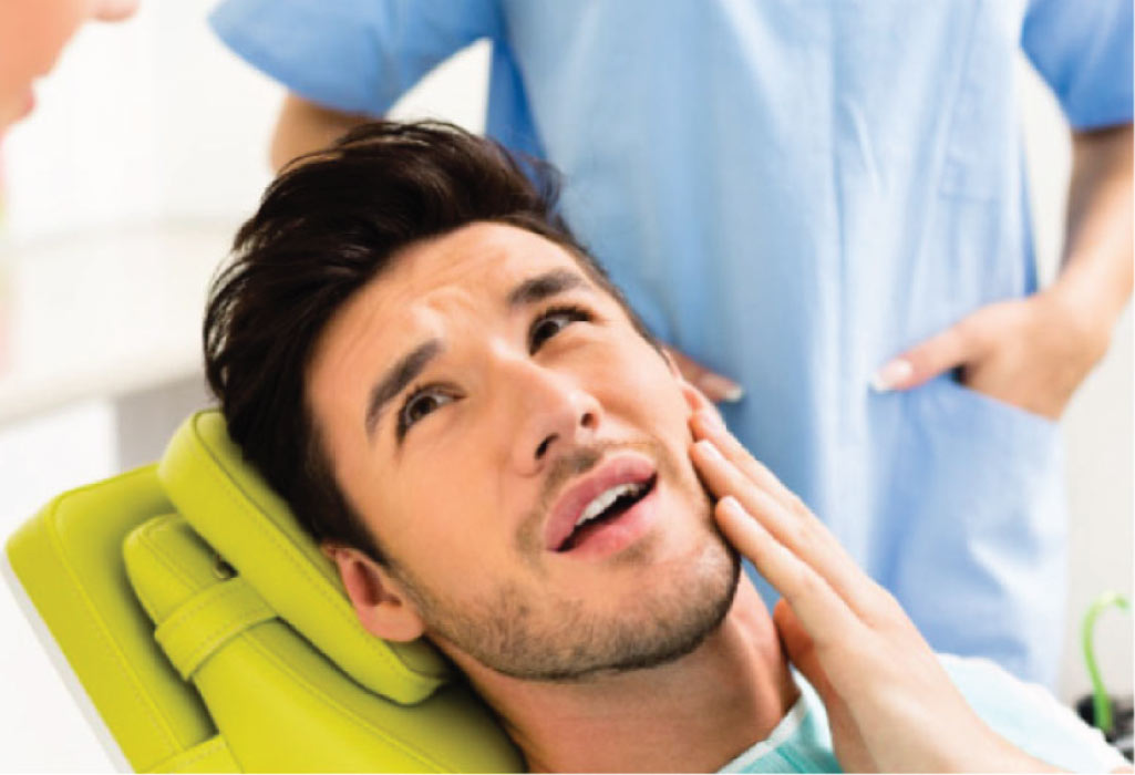 young man in the dentist chair holds his cheek with root canal pain