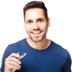 man holds his clear aligner and smiles after finding out about bruxism relief